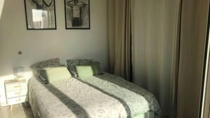 A bedroom with a bed, two framed artworks, a nightstand, and a window with curtains. - Whole apartment in Six-Fours-les-Plages, France (Six-Fours-les-Plages)