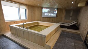 A wooden spa room with a large bathtub, a television screen, and a massage table. - Amor Hotel (Changwon)