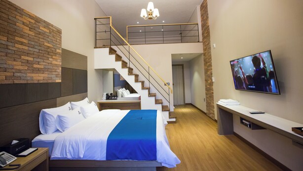 A modern hotel room with a large bed, a TV mounted on the wall, a staircase, and a wooden floor. - Amor Hotel (Changwon)