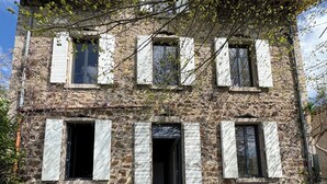 A stone building with multiple windows and a front door, surrounded by greenery and flowers. - House 1880 (Annonay)