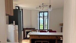 A modern kitchen with a central island, wooden cabinets, and a large window providing natural light. - House 1880 (Annonay)