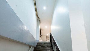 Een smalle trap met een zwarte leuning die leidt naar een kamer met witte muren en een plafondlamp.