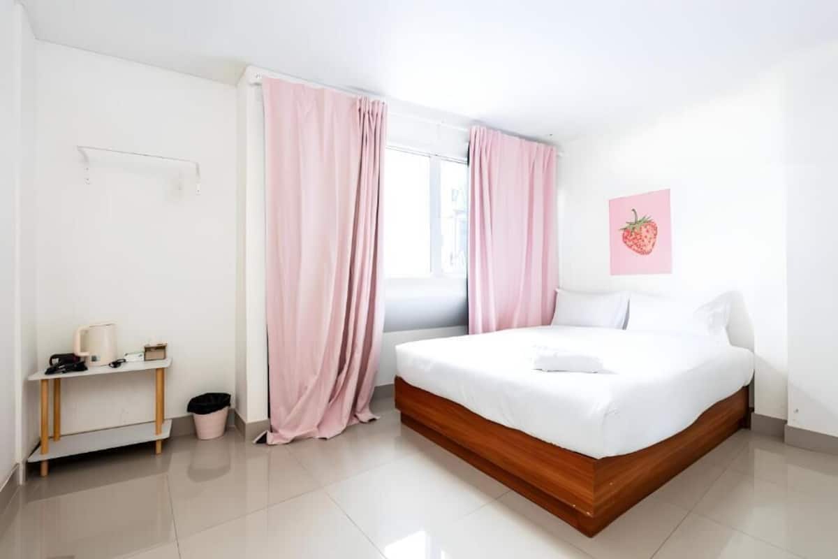 A bedroom with a bed, a bedside table, a lamp, and a trash bin.