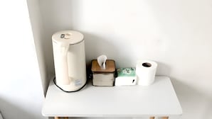 Een wit bureau met een witte beker, een pak zakdoekjes en een rol toiletpapier.