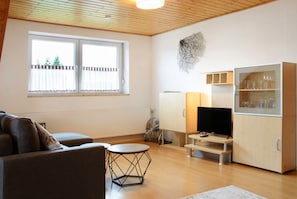Moderni olohuone, jossa on sohva, pyöreä sohvapöytä, televisio ja lasikaappi.