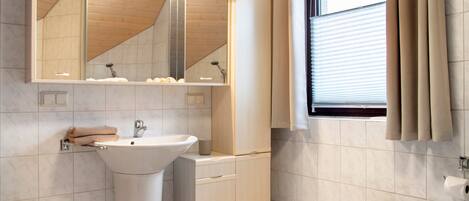 Ein Badezimmer mit Waschbecken, Spiegel, Schrank, Toilette und einem Fenster mit Vorhängen.
