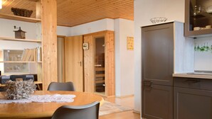 A wooden dining table with chairs, a kitchen area with cabinets, and a wooden door with a glass panel.