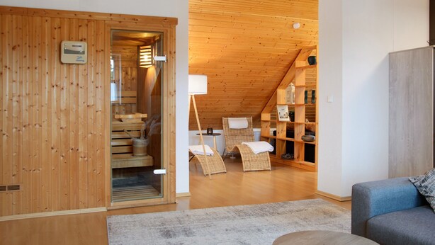 A wooden interior with a loft bedroom, a sofa, and a wicker chair.