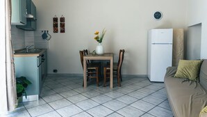 Ein gemütlicher Wohnbereich mit Küchenzeile, einem Esstisch mit Stühlen, einer Couch und einem kleinen Kühlschrank.