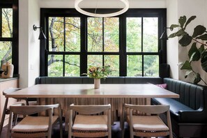 A dining area with a wooden table, four chairs, a bench, and a large window with a view of trees.