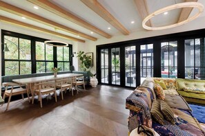 Una habitación amplia con una mesa de comedor de madera y sillas, un sofá verde, y ventanas grandes que ofrecen vistas al exterior.