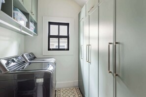 A laundry room with a washing machine, dryer, and a window above a cabinet.