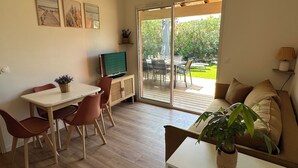 Una sala de estar con televisor, un comedor con sillas, un sofá y un ventanal corredera que da a un patio exterior.