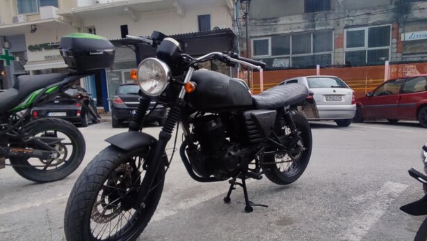 Une moto est garée sur une surface pavée, avec des bâtiments en arrière-plan.