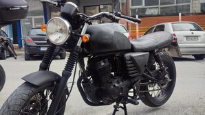 Une moto est garée sur une surface pavée, avec des bâtiments en arrière-plan.