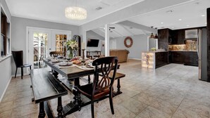 Un vaste espace dédié à la salle à manger, avec une longue table, des chaises et un lustre. On y trouve également une cuisine équipée d’appareils modernes et dotée d’un grand îlot central.