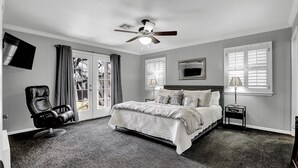 Une chambre à coucher avec un lit, une chaise, un ventilateur de plafond, une télévision et une fenêtre.