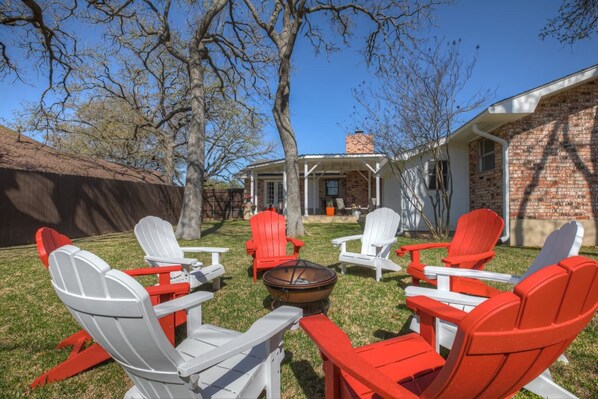 Patio trasero con sillas Adirondack, una fogata y una casa de ladrillo.