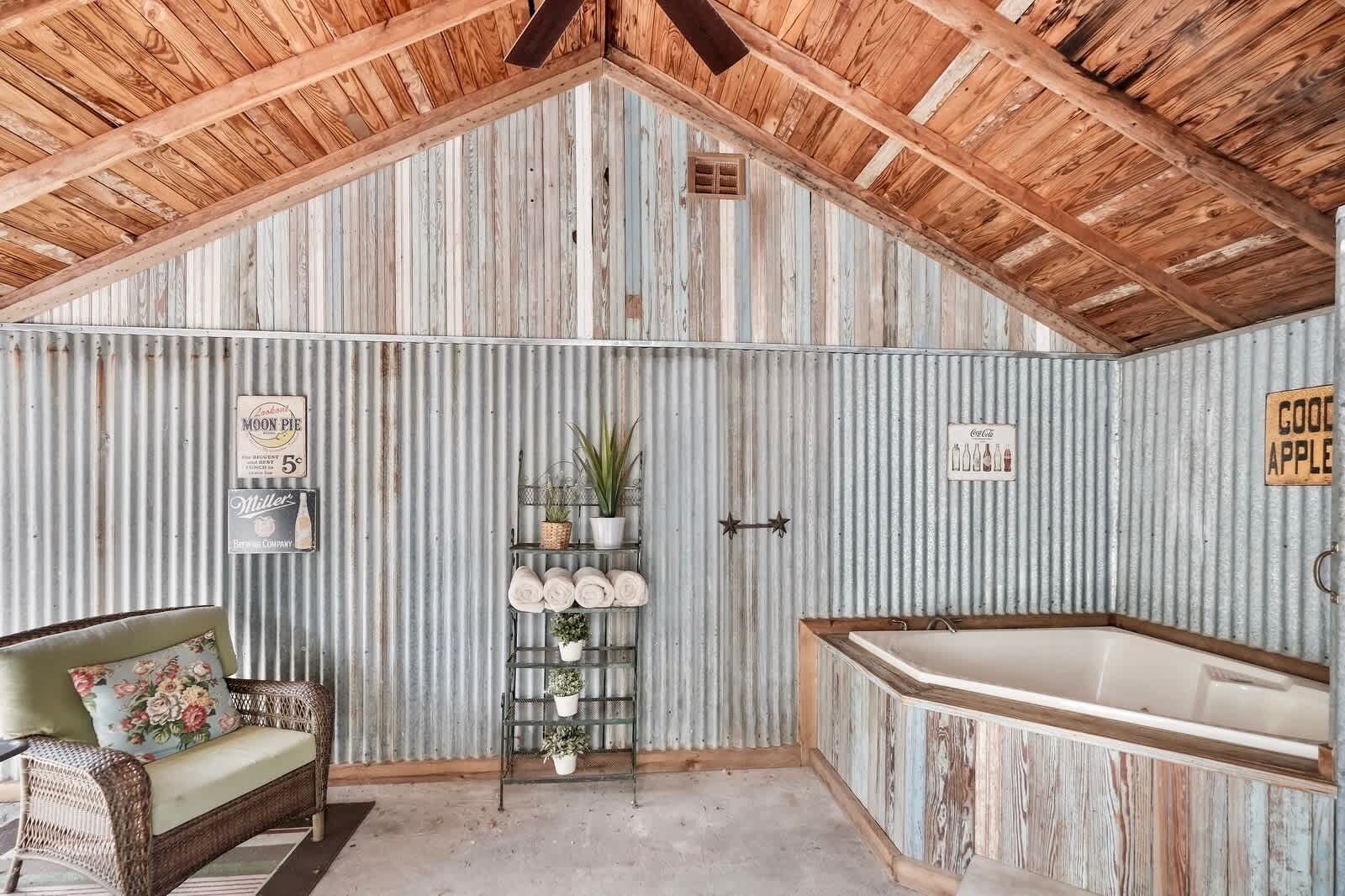Ein rustikales Badezimmer mit Holzbalkendecke, einer Badewanne und einem Regal mit Handtüchern und Pflanzen.