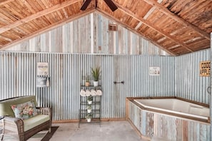 A rustic bathroom with a wooden ceiling, a bathtub, and a shelf with towels and plants. - Bungalow on College - Close to Main, Outdoor oasis (Fredericksburg)