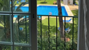 A view through a window with a metal grill, featuring a swimming pool, green lawn, and buildings in the background. - Penthouse El Presidente Estepona 400 meters beach (Estepona)