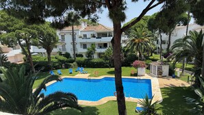 A swimming pool surrounded by lush greenery and palm trees, with a white building in the background. - Penthouse El Presidente Estepona 400 meters beach (Estepona)