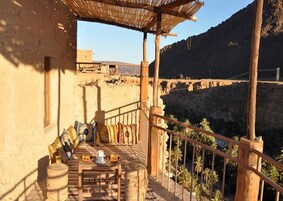 Un balcón de madera con mesa y sillas, con vistas a un paisaje montañoso.