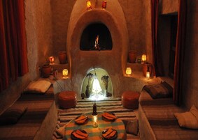 Una habitación rústica con chimenea de piedra, una mesa con velas y un banco.
