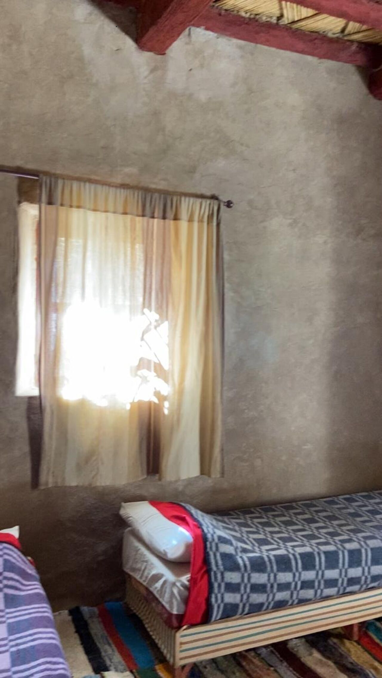 A small, simple room with a single bed, a window with curtains, and a plain wall.