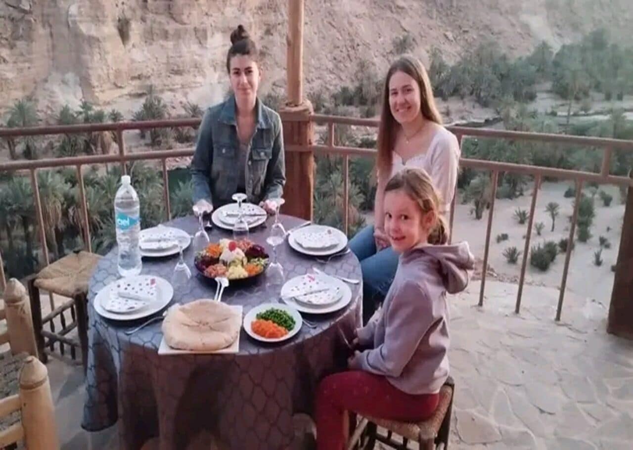 Una mesa de comedor con platos, cubiertos y una botella de agua en un balcón con vistas a un paisaje montañoso.