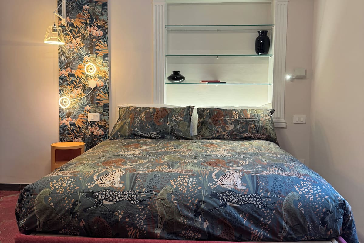 Un dormitorio con una cama grande, un estante en la pared y un papel tapiz estampado.