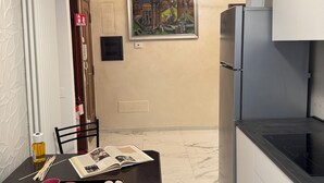 Eine moderne Küche mit einem Kühlschrank, einem Esstisch mit einer Zeitschrift und rosa Tassen, sowie einem Gemälde über dem Tisch.
