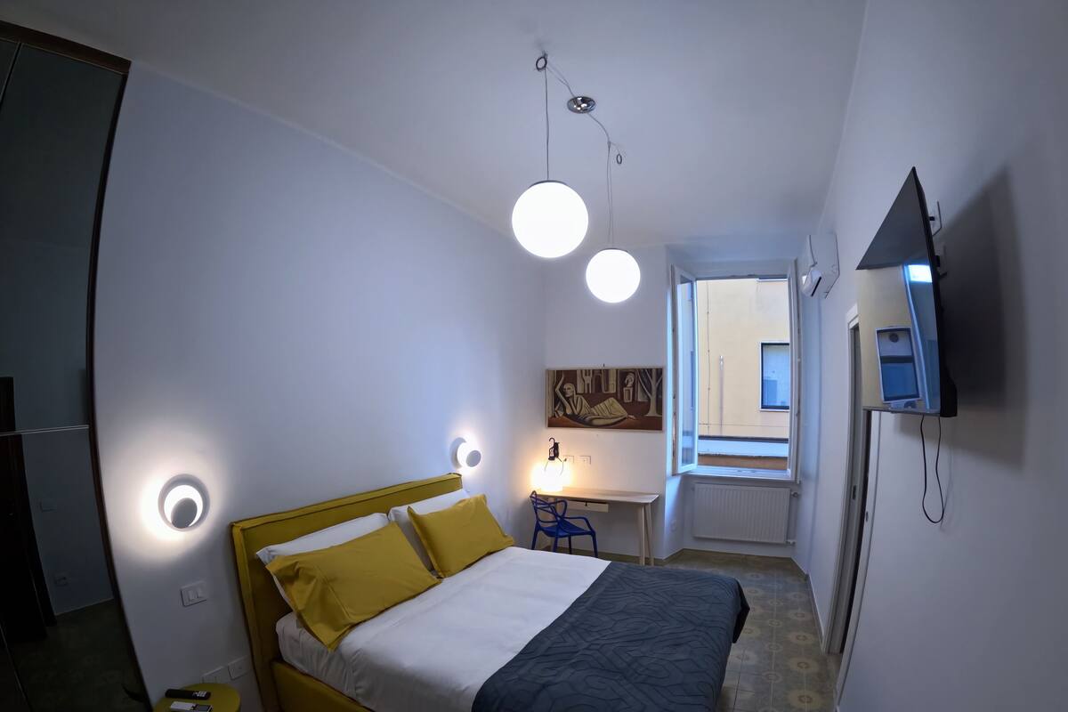Un dormitorio con cama, mesita de noche y televisor montado en la pared.
