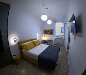 Un dormitorio con cama, mesita de noche y televisor montado en la pared.