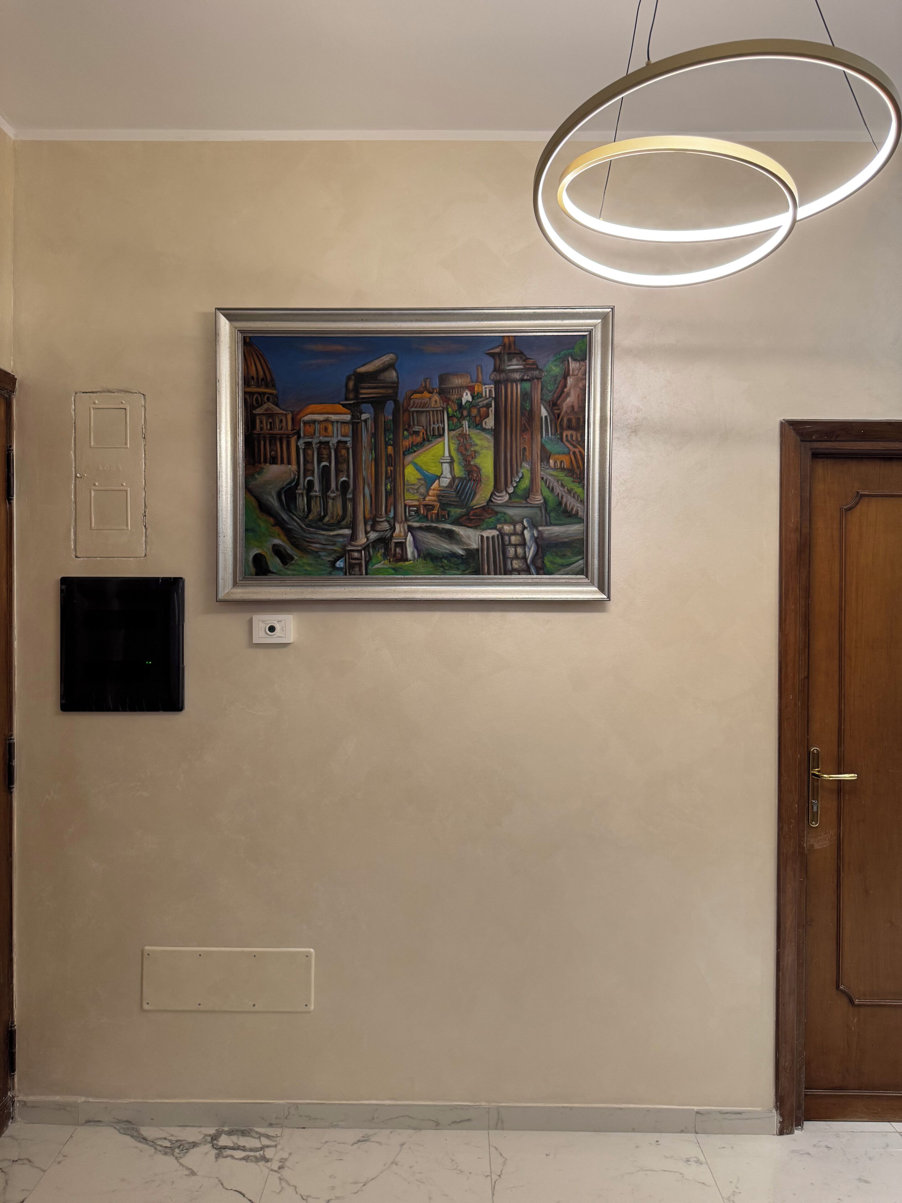 A framed painting of ancient ruins on a beige wall, a modern light fixture, a door, and a wall-mounted light switch.