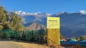 A sign for Kedar Resorts with a view of snow-capped mountains in the background.