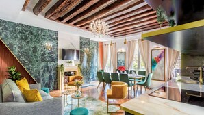 A modern living room with a fireplace, green and yellow chairs, a dining area with a table and chairs, and a kitchen with a stainless steel sink. - Merveil Luxury Suites - Marais - Antoine I-II (Paris)
