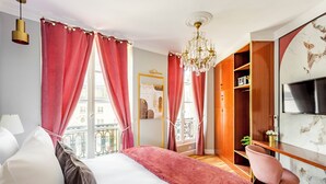 A modern bedroom with a large bed, red curtains, a chandelier, a desk with a chair, and a TV on the wall. - Merveil Luxury Suites - Marais - Antoine I-II (Paris)