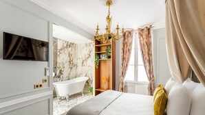 A bedroom with a bed, a TV, a bathtub, and a chandelier. - Merveil Luxury Suites - Marais - Antoine I-II (Paris)
