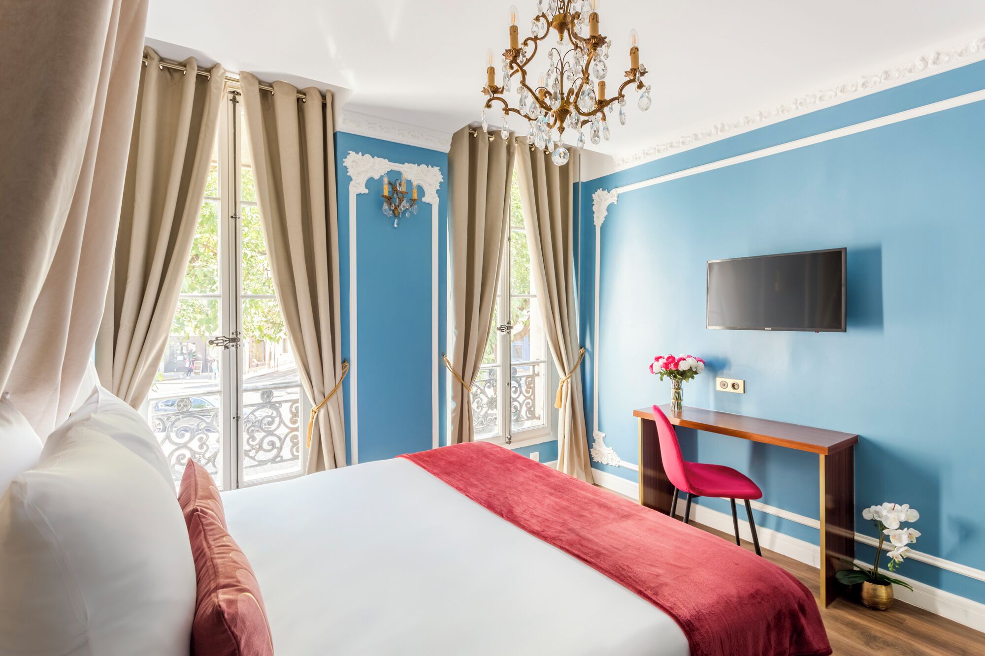 Camera d'albergo con un letto, una scrivania, una sedia, una televisione e un balcone con tende.