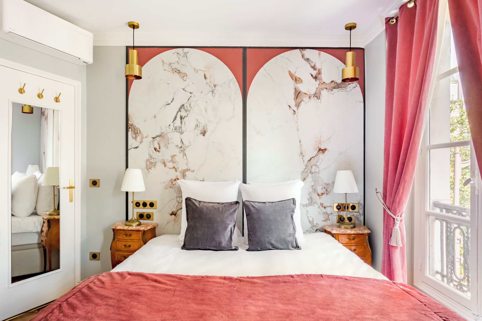 A bedroom with a large bed, two bedside tables with lamps, a mirror, and a marble-patterned headboard.