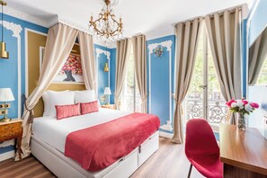 A bedroom with a large bed, a desk, and a chair. There is a window with curtains, a chandelier, and a decorative wall. - Merveil Luxury Suites - Marais - Antoine I-II (Paris)