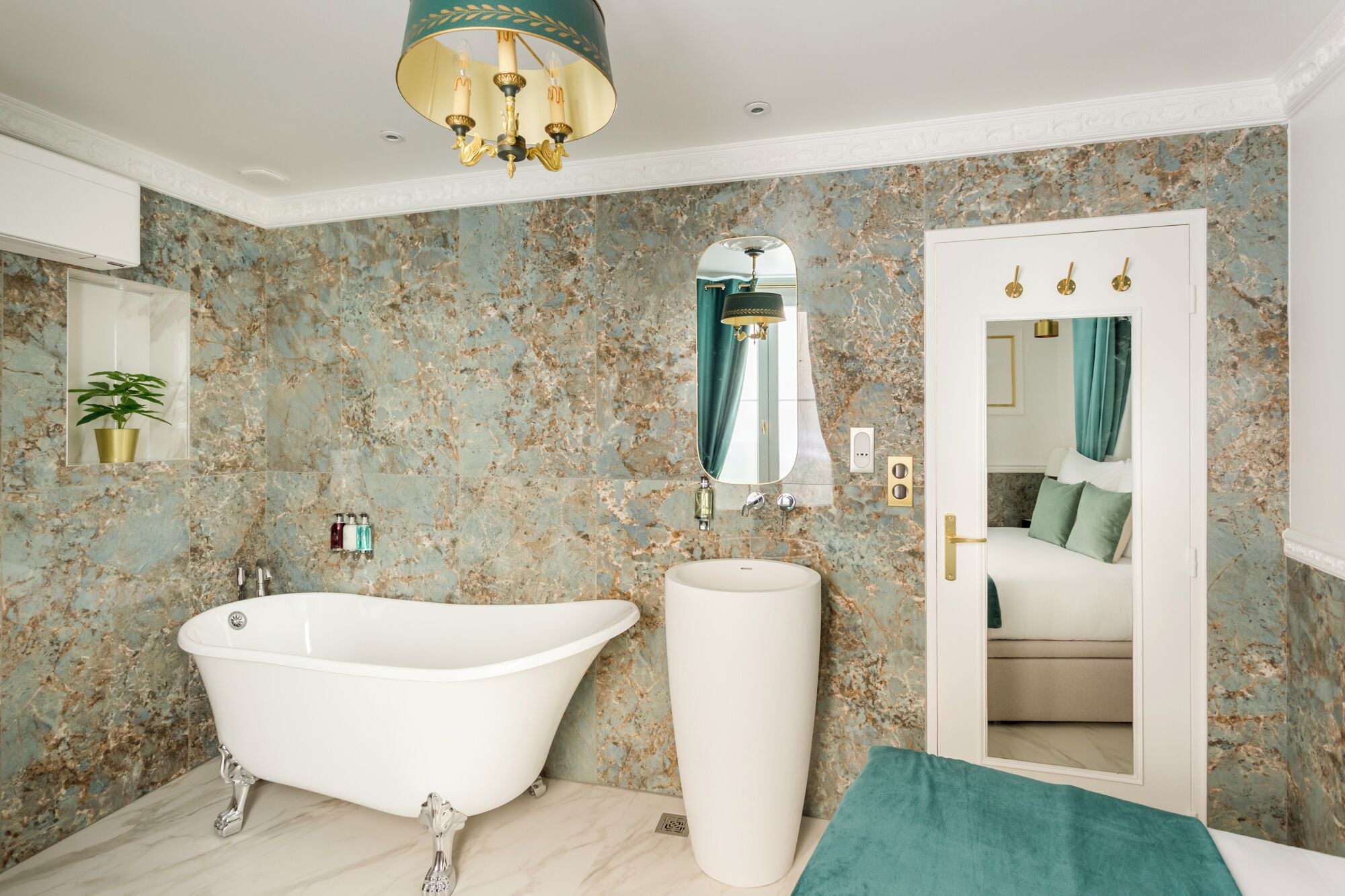 A bathroom with a freestanding bathtub, a large mirror, and a door leading to a bedroom.