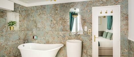 A bathroom with a freestanding bathtub, a large mirror, and a door leading to a bedroom.