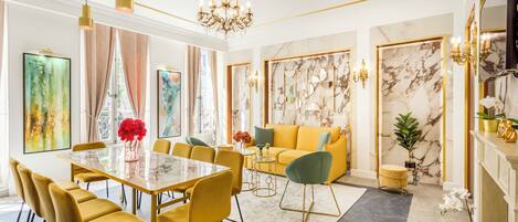 Una sala de estar moderna con una mesa de comedor de vidrio, sillas amarillas, un sofá amarillo y una pared de acento de mármol.