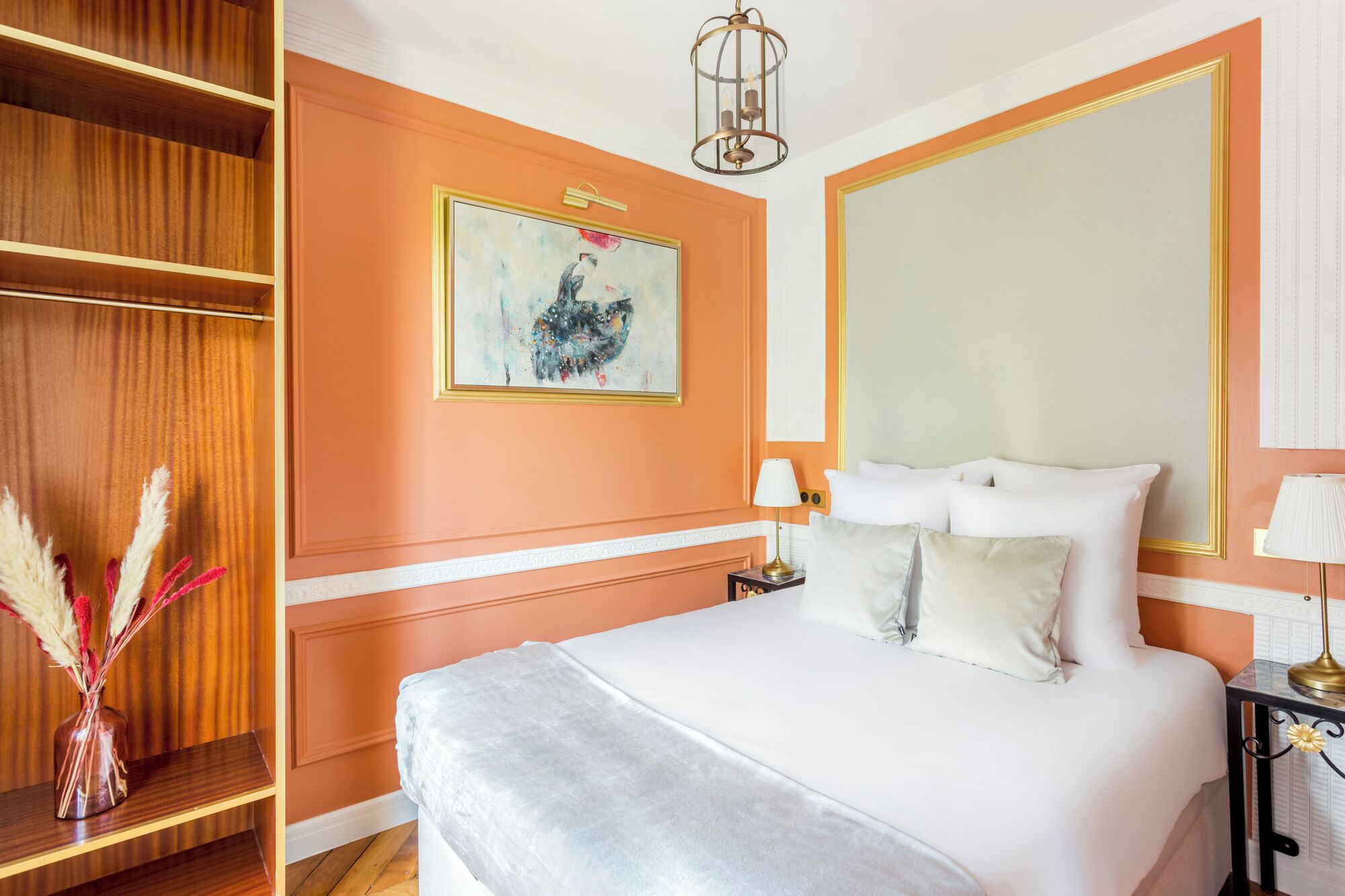 A hotel room with a large bed, a nightstand with lamps, a wardrobe, and a painting on the wall.