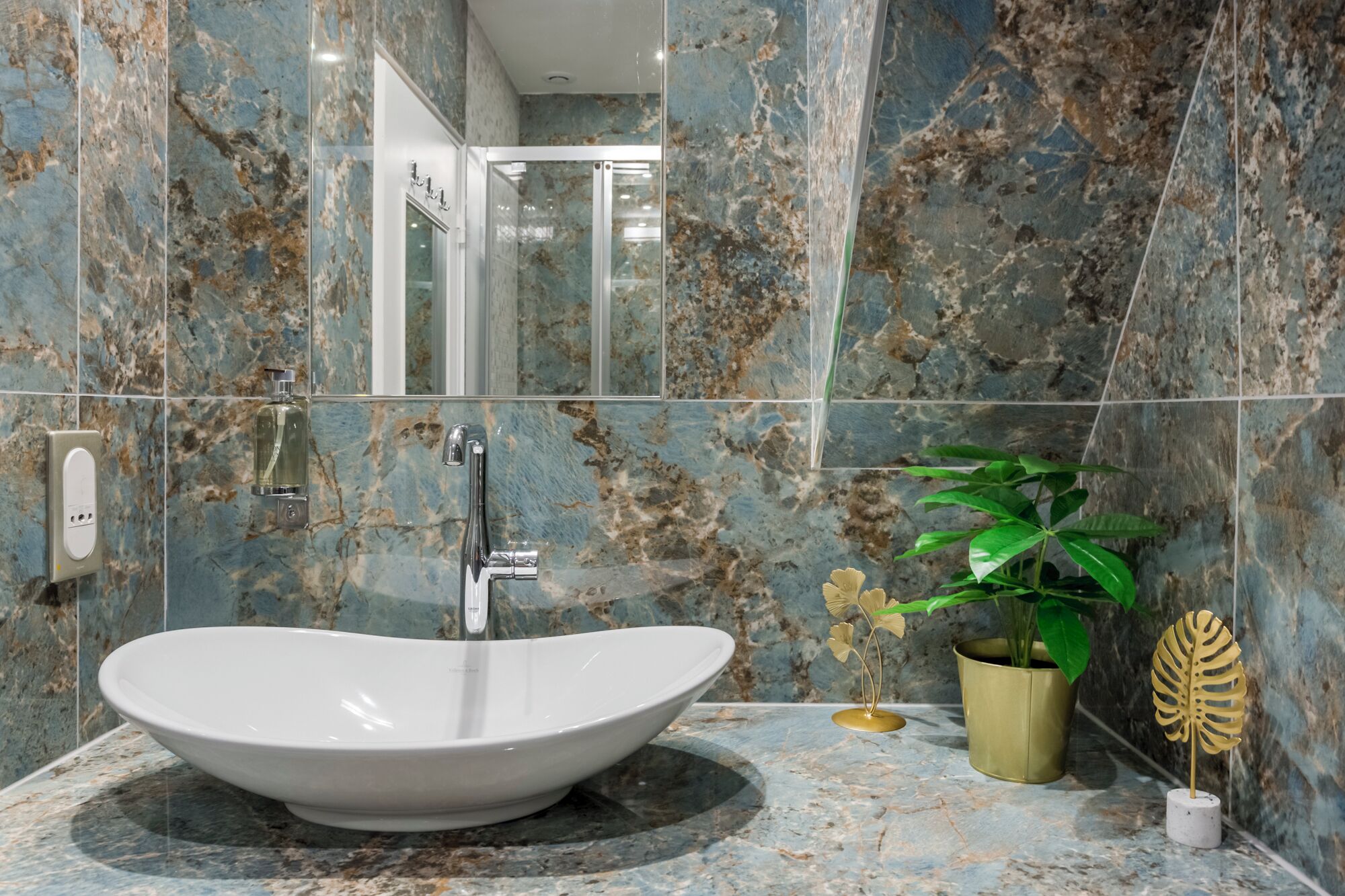 A bathroom with a large, oval sink, a glass shower enclosure, and a potted plant.