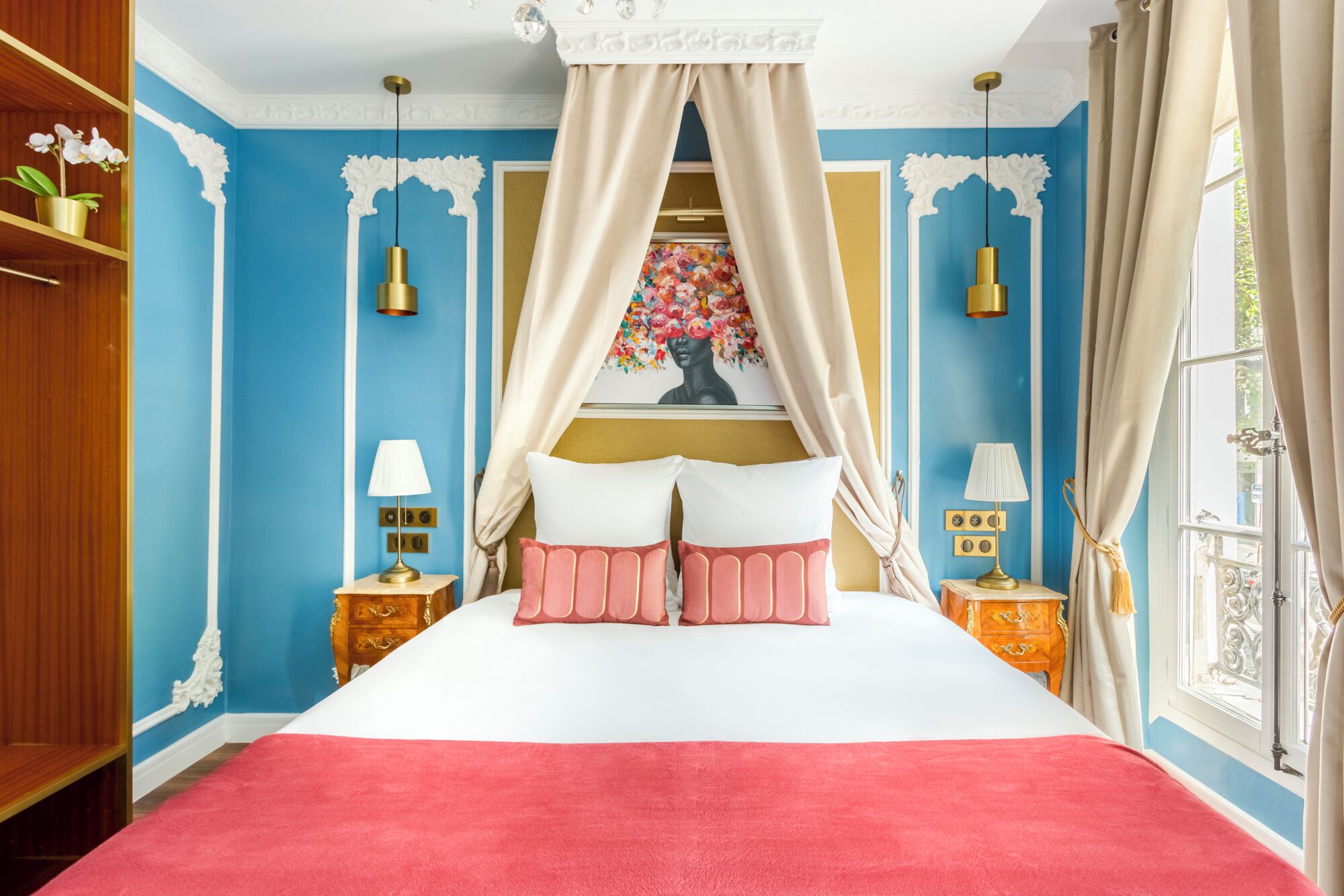 Una camera da letto con un letto a baldacchino, due comodini con lampade, un quadro floreale sopra il letto e vista all'esterno attraverso una finestra.