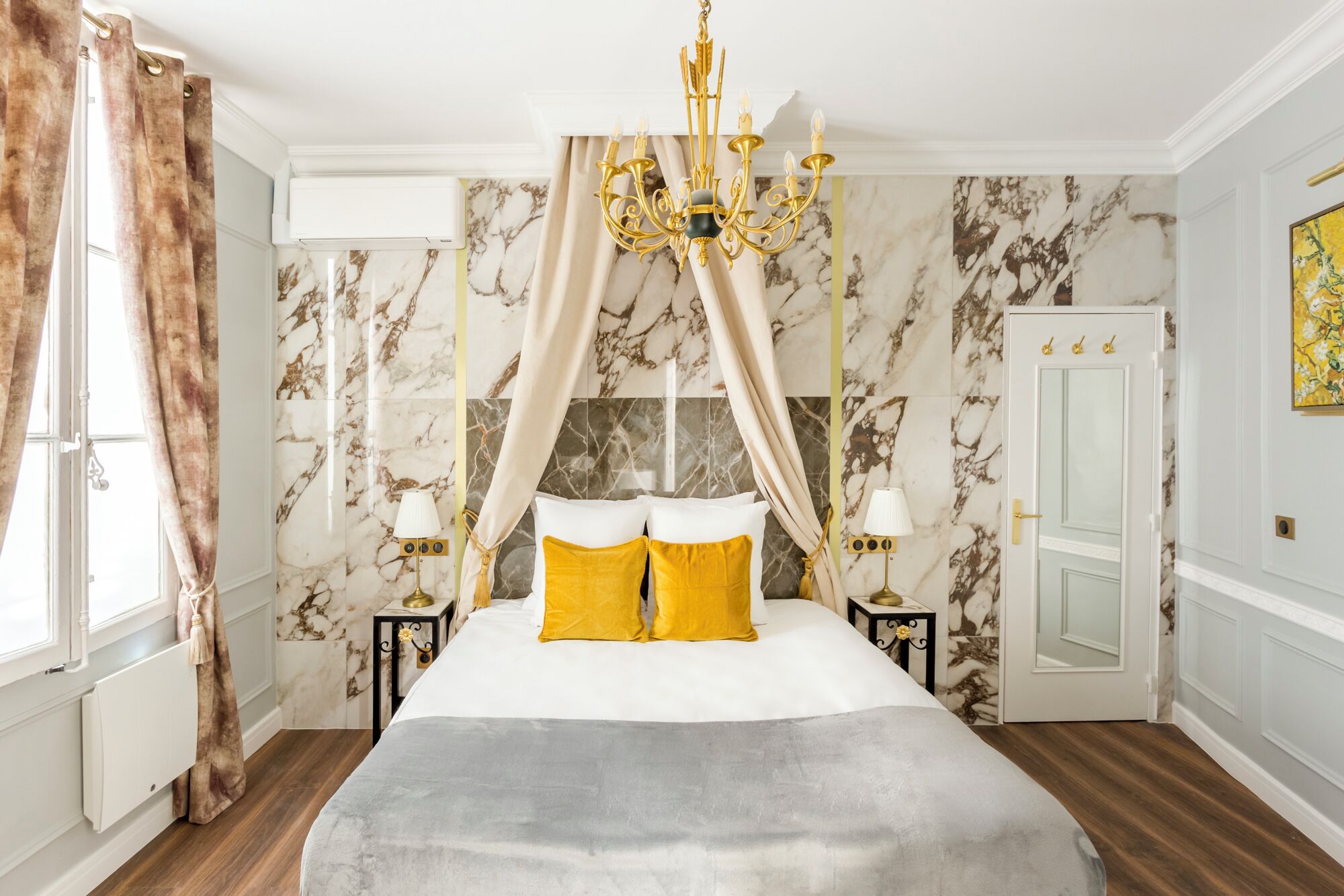 A bedroom with a large bed, a chandelier, marble walls, and a door with a mirror.