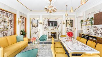 A modern living room with a marble fireplace, a dining area with yellow sofas and a marble table, and a kitchen with a marble countertop.